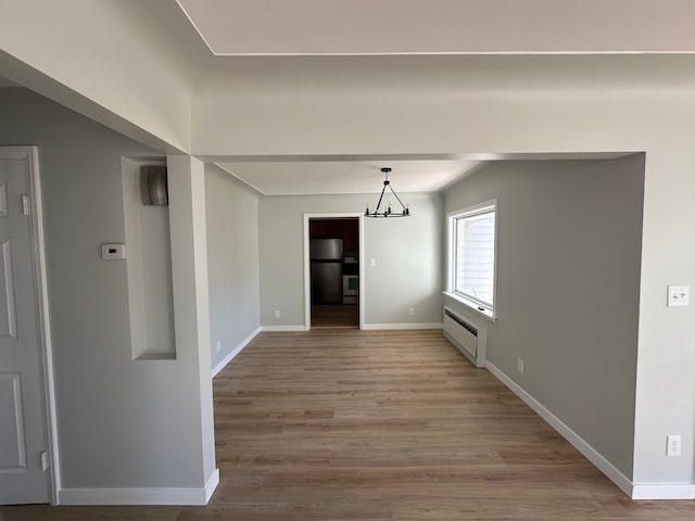 unfurnished room featuring a notable chandelier, light wood-type flooring, baseboards, and a baseboard radiator