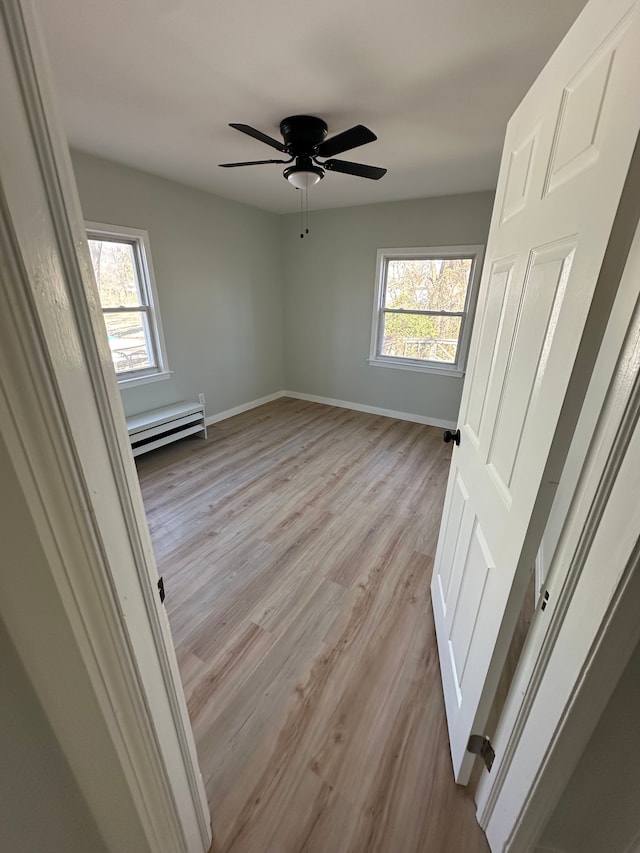 unfurnished bedroom with a baseboard heating unit, multiple windows, light wood-style floors, and baseboards