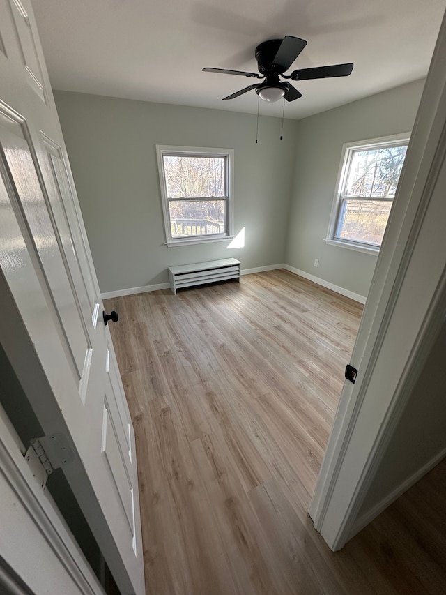 unfurnished bedroom with a baseboard heating unit, light wood-style flooring, baseboards, and ceiling fan