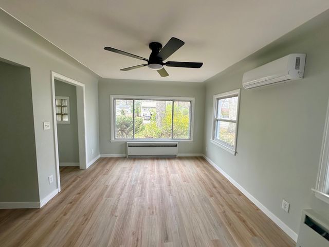 4120 Lotus Dr, Waterford, MI 48329 - empty room featuring an AC wall unit, a baseboard heating unit, healthy amount of natural light, and wood finished floors