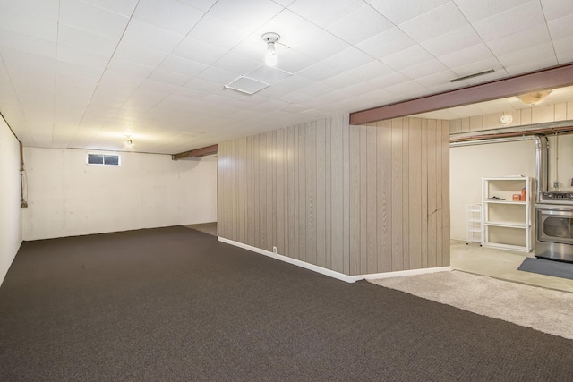 finished below grade area featuring visible vents, carpet flooring, a wood stove, and wooden walls