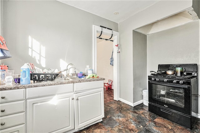 kitchen with stone finish flooring, white cabinets, light countertops, baseboards, and black range with gas stovetop