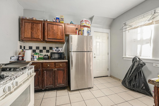 kitchen featuring light tile patterned floors, white gas stove, freestanding refrigerator, black microwave, and tasteful backsplash