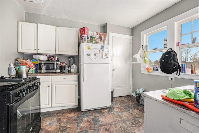 kitchen featuring stainless steel microwave, stone finish flooring, freestanding refrigerator, gas stove, and white cabinetry