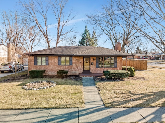 ranch-style home featuring brick siding, a chimney, a front yard, and a shingled roof