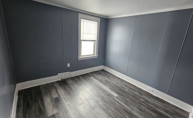 empty room with a decorative wall, dark wood-style floors, visible vents, and baseboards