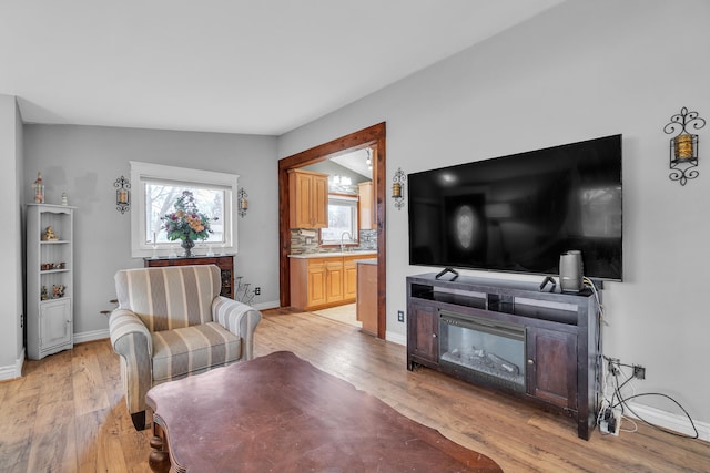 living room featuring light wood-style flooring, baseboards, and vaulted ceiling