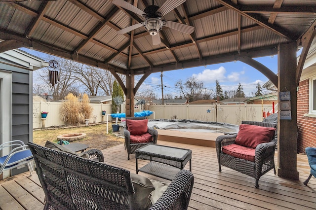 wooden terrace with a gazebo, an outdoor living space with a fire pit, a fenced backyard, and a ceiling fan