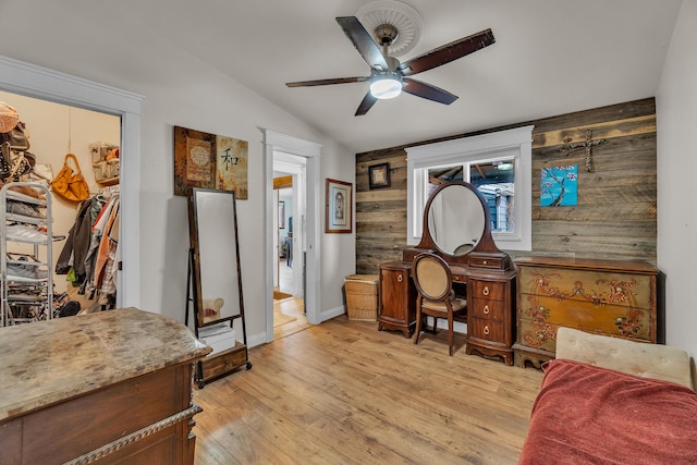 home office featuring lofted ceiling, wooden walls, a ceiling fan, and light wood finished floors