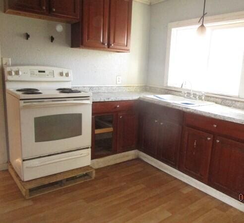 kitchen with light stone counters, light wood finished floors, a sink, hanging light fixtures, and electric stove