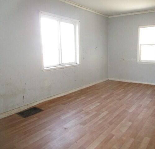 spare room featuring crown molding, light wood-style flooring, baseboards, and visible vents