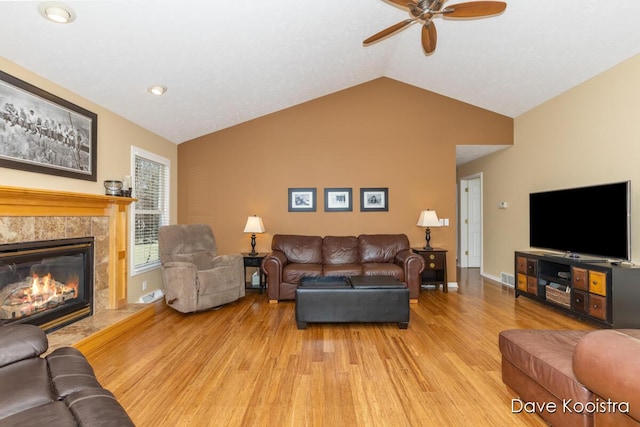 living area with a high end fireplace, visible vents, baseboards, vaulted ceiling, and light wood-style flooring