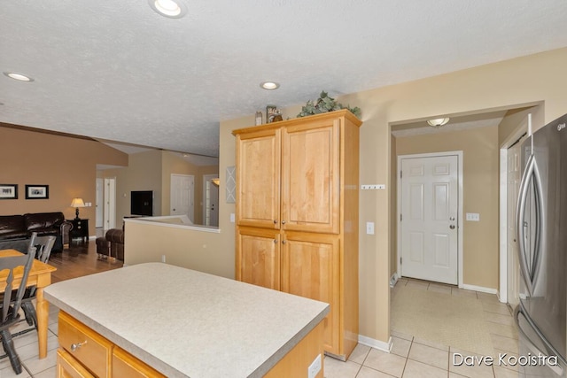 kitchen featuring a kitchen island, freestanding refrigerator, light tile patterned flooring, light countertops, and lofted ceiling