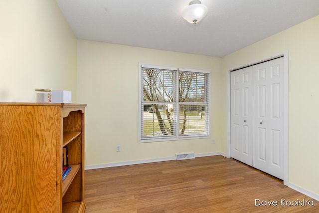 unfurnished bedroom featuring visible vents, baseboards, a closet, and wood finished floors