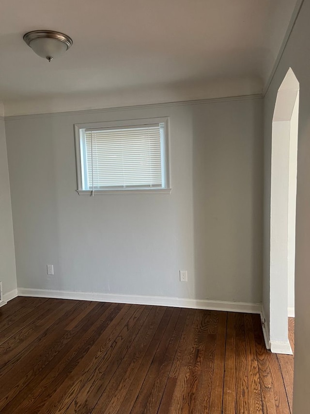 unfurnished room with baseboards, arched walkways, and dark wood-type flooring