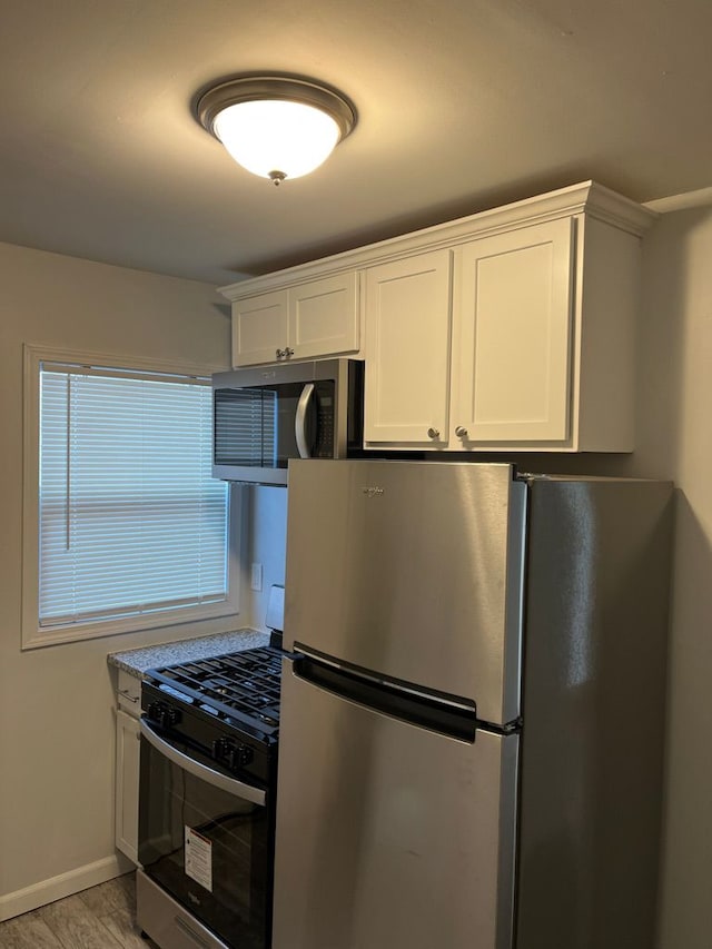 kitchen with white cabinetry, light wood finished floors, baseboards, and appliances with stainless steel finishes