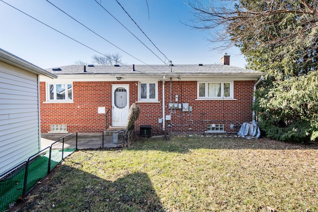 back of property with a lawn, entry steps, a shingled roof, brick siding, and a chimney