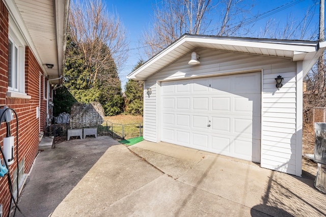 detached garage featuring concrete driveway and fence