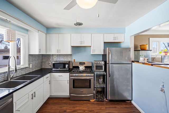 kitchen with dark wood finished floors, a sink, appliances with stainless steel finishes, white cabinetry, and dark countertops