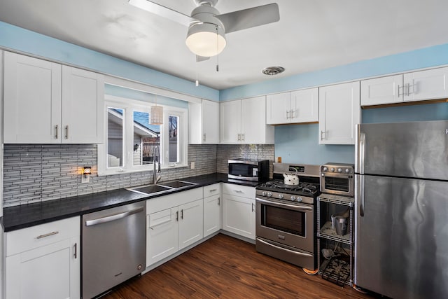 kitchen featuring dark wood-type flooring, a sink, dark countertops, appliances with stainless steel finishes, and white cabinets