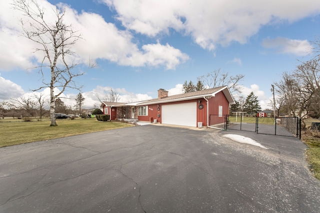 view of front of home with aphalt driveway, a front yard, a chimney, a garage, and a gate