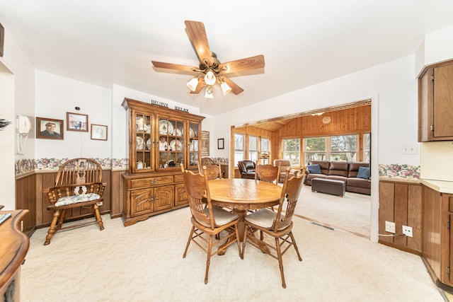 dining area featuring wainscoting, wood walls, light colored carpet, and ceiling fan