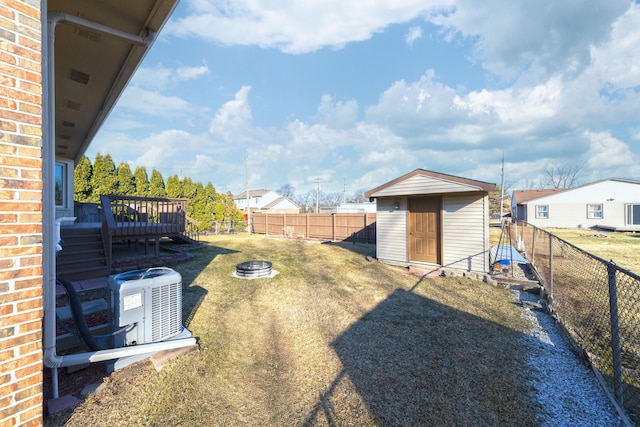 view of yard with an outdoor fire pit, a wooden deck, central AC unit, a fenced backyard, and an outbuilding