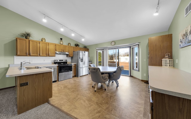 kitchen with a peninsula, lofted ceiling, stainless steel appliances, light countertops, and under cabinet range hood