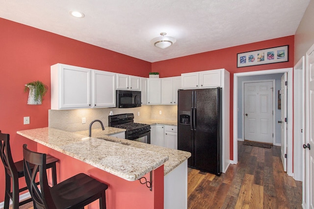 kitchen featuring a peninsula, a sink, black appliances, white cabinetry, and tasteful backsplash