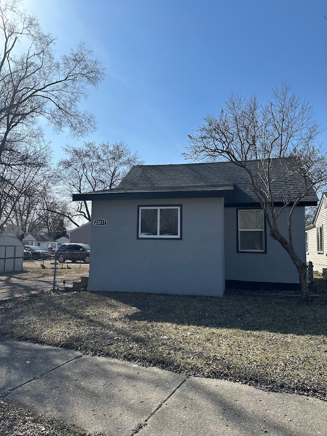 view of side of home with fence, roof with shingles, and stucco siding