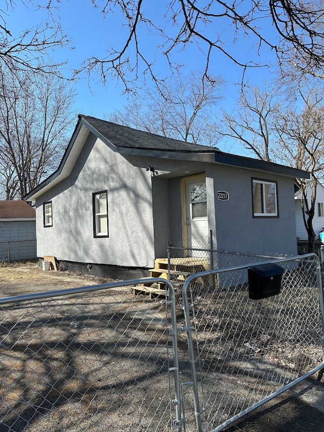 view of front of property featuring roof with shingles, a gate, a fenced front yard, and stucco siding