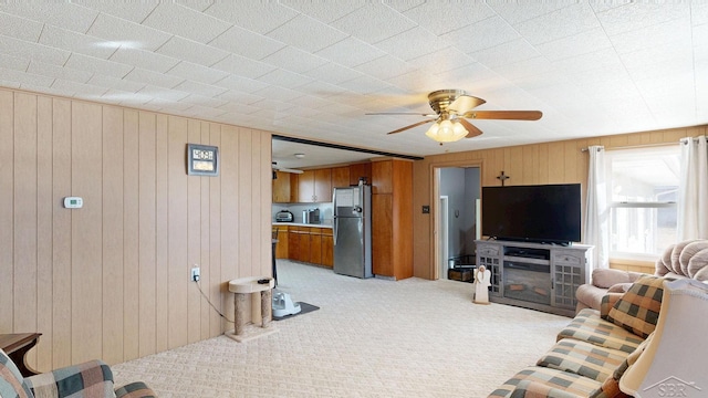 living room featuring wooden walls, a ceiling fan, and light carpet