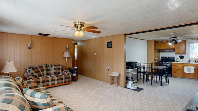 living area featuring light carpet, wooden walls, and a ceiling fan