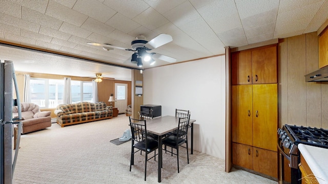 dining space with baseboard heating, wood walls, crown molding, light colored carpet, and ceiling fan