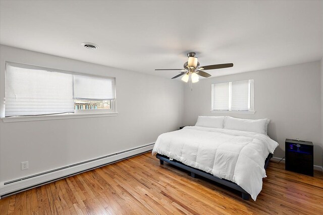 bedroom with wood finished floors, visible vents, baseboard heating, and ceiling fan