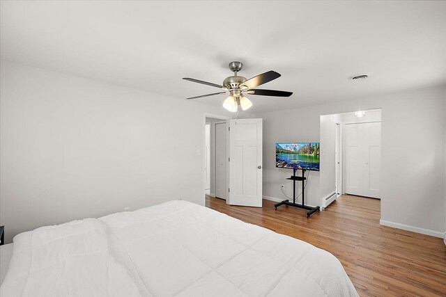 bedroom featuring baseboards, wood finished floors, visible vents, and a baseboard radiator