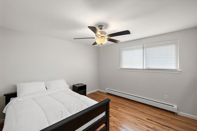 bedroom featuring wood finished floors, a ceiling fan, baseboards, and a baseboard radiator