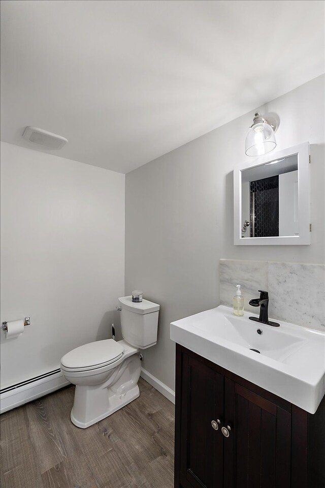 bathroom featuring vanity, wood finished floors, a baseboard heating unit, toilet, and tasteful backsplash