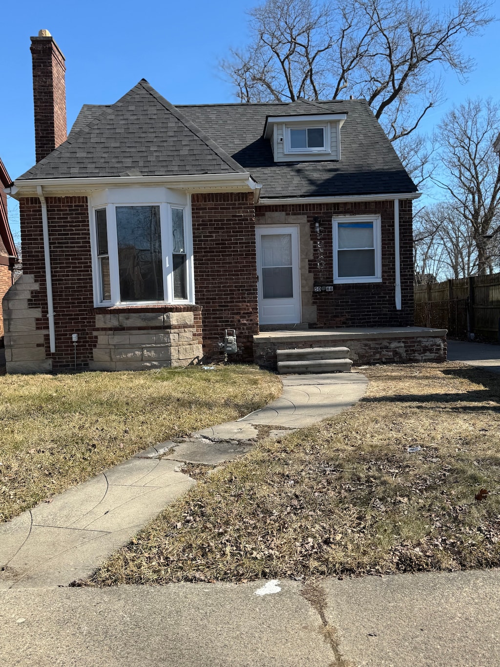 bungalow featuring fence, brick siding, roof with shingles, and a chimney