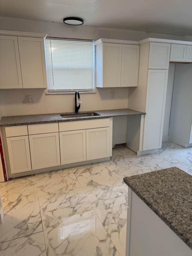 kitchen featuring marble finish floor, dark stone counters, and a sink