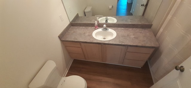 half bath with toilet, wood finished floors, and vanity