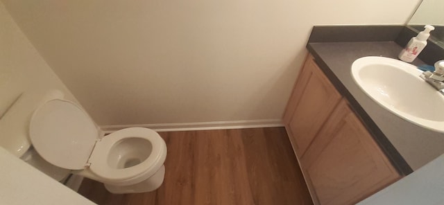 half bathroom with toilet, vanity, baseboards, and wood finished floors