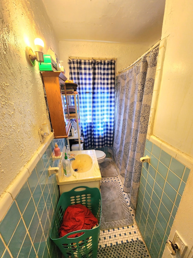 full bathroom with vanity, wainscoting, tile walls, toilet, and a textured wall