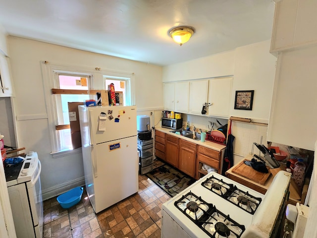 kitchen with a sink, white appliances, brown cabinetry, brick floor, and washer / dryer