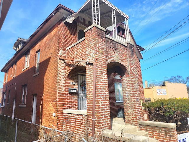 view of side of home featuring brick siding, a balcony, and fence