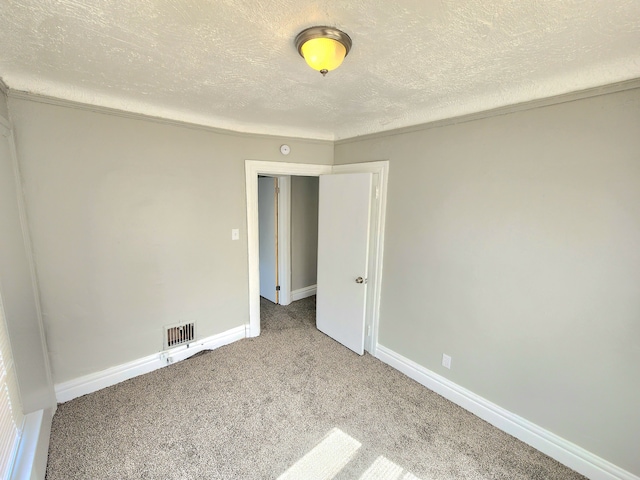 empty room featuring visible vents, carpet flooring, a textured ceiling, and baseboards