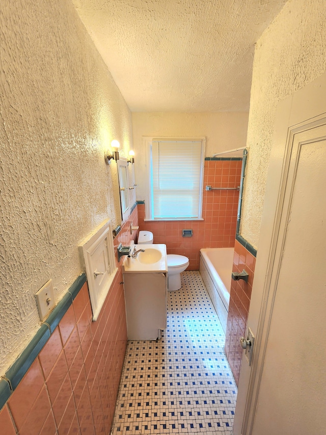 full bathroom with a textured ceiling, toilet, and a textured wall