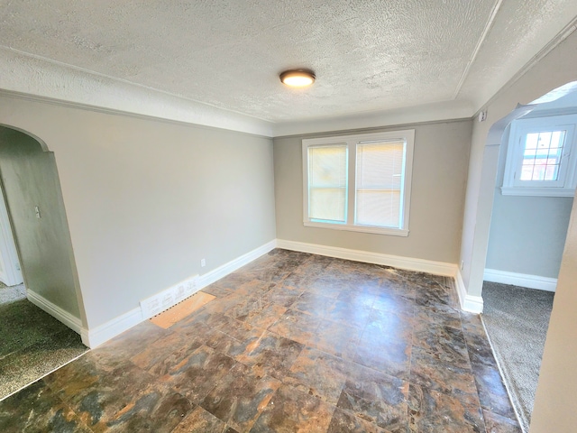 empty room featuring arched walkways, a textured ceiling, and baseboards