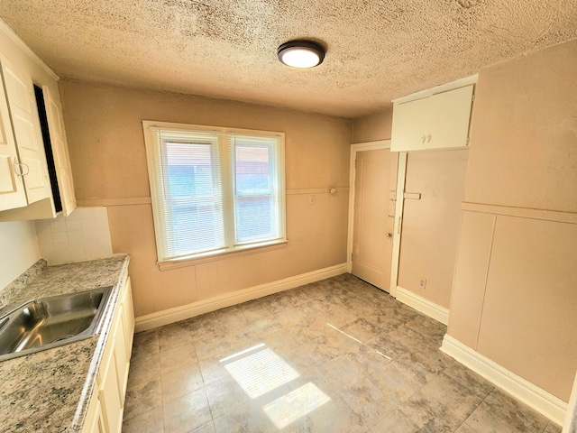 kitchen with a wainscoted wall, a sink, light countertops, white cabinets, and a textured ceiling