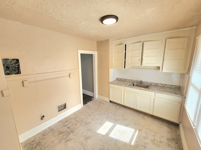 kitchen featuring visible vents, a sink, light stone counters, a textured ceiling, and white cabinetry